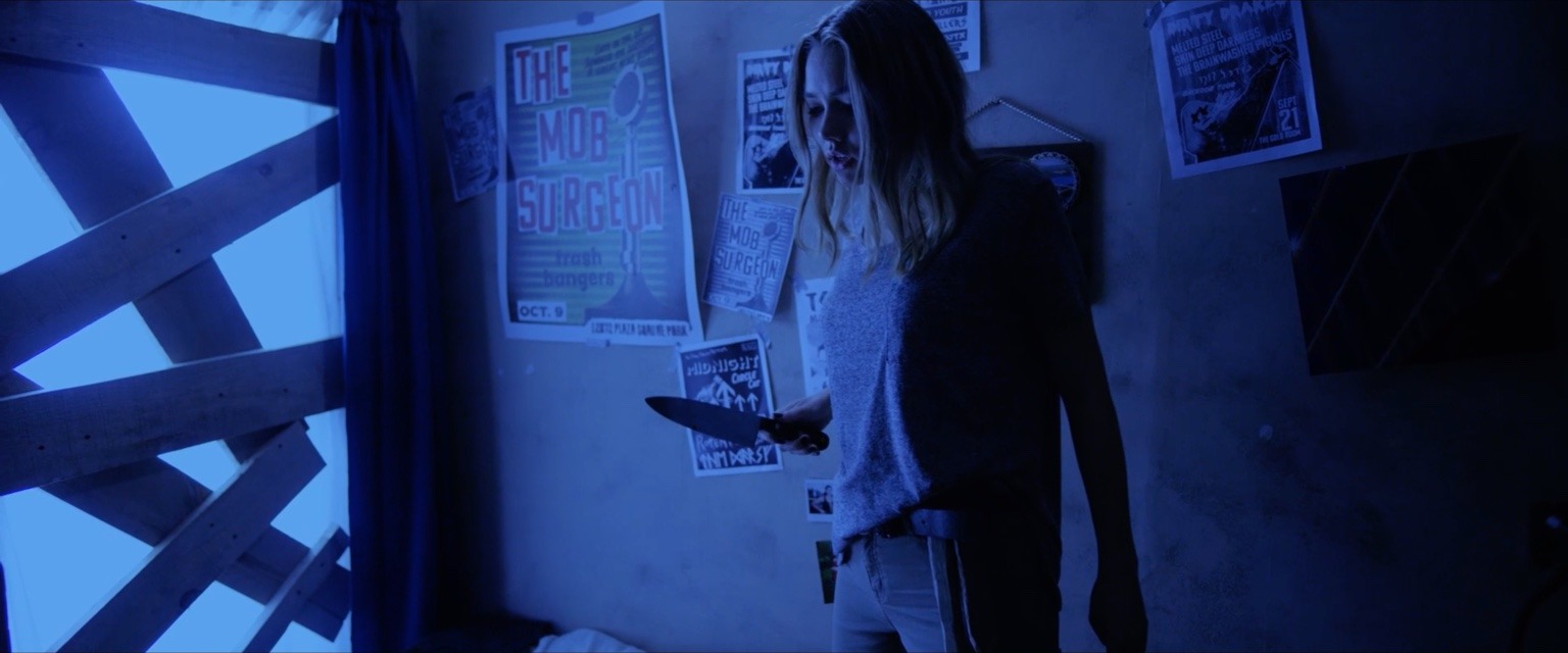 A young woman holding a knife in a blue-lit room